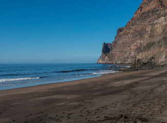 Fototapeta na wymiar View of empty sand beach Playa de Guigui with rocky cliffs in west part of the Gran Canaria island, accessible only on foot from Barranco de Guigui Grande gorge or by boat. Canary Islands, Spain