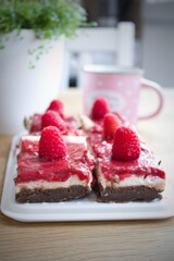 Raspberry cheescake brownies pieces with fresh berries and coffee on the table. Good morning. Sweet baked homemade breakfast or dessert of three layers.