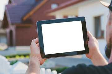 Close-up of a tablet in the hands of a man, on the background of the house.