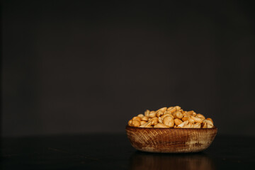 Roasted peanuts in wooden bowl on black background with empty space in the frame