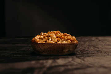 Wooden bowl of roasted peanuts in the middle of the frame placed on synthetic fabric