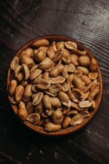 Detailed, top view photo of rosted peanuts with salt flakes on top of them placed in wooden bowl on a wooden table