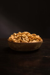Vertical photograph of roasted peanuts in wooden bowl on a black background