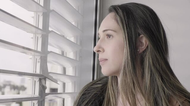 Woman looking out the window shutters smiling and waving to friends outside. happy Positive beautiful morning lady looking out the blinds to the street. saying hi to lover outside. closer up