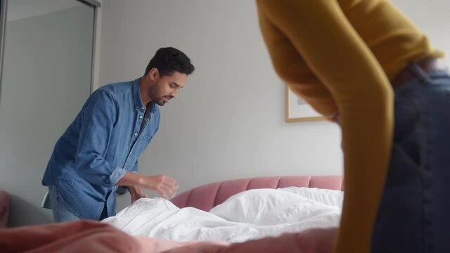 Young couple sharing domestic chores and making bed at home together - shot in slow motion