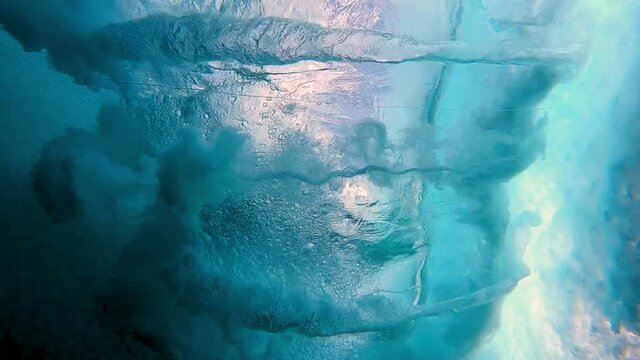 Underwater looking up through a crashing ocean wave with bright sunlight, illuminated bubbles, and the many deep blue hues of the clear water - Oahu, Hawaii