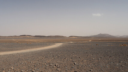 Desert plain landscape with car trail. Landscape of rocky desert with 4x4 car trail. Grey gravel, yellow sand, plain horizon with low hills and clear sky.