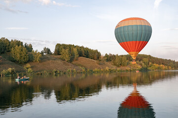 Naklejka premium a balloon with people in a basket hovers over the hilly terrain above the water