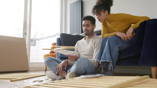 Young couple sitting on sofa in lounge at home reading instructions for flat pack furniture assembly