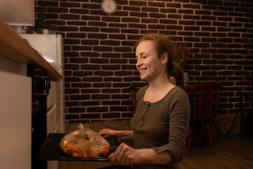 Cheerful housewife taking roasted chicken out of oven at home