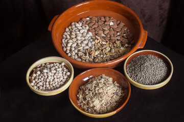 A large clay pot with a variety of dried fruits along with small artisan soup plates filled with lentils, chickpeas, and toasted flakes of rice, whole wheat, and barley with chocolate shavings.