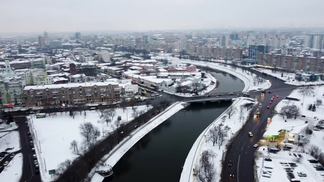 Winter snowy day aerial view to downtown. Fly above dark water of river Kharkov, streets with cars driving and a bridge in Kharkiv, Ukraine. Urban city wintery patterns