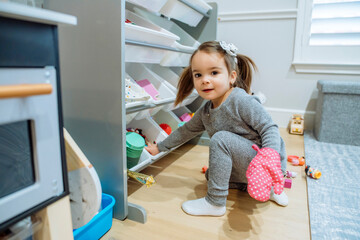 happy toddler girl pulling toys out of bins surrounded by messy toys on floor