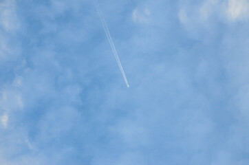 Airplane in blue sky among the clouds with plane trails. Travel.
