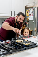 Dad making pancakes with toddler daughter