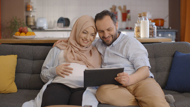 A pregnant Muslim woman wearing a headscarf and her husband use a tablet computer to exchange babies online. Online baby shopping concept. - Powered by Adobe