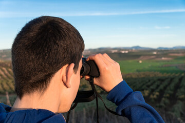 Unrecognized young boy standing in the mountain looking the landscape using binoculars. Selective focus.