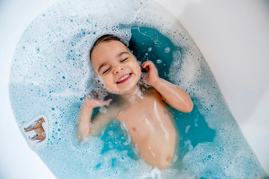 Happy, smiling girl taking bubble bath in bathtub