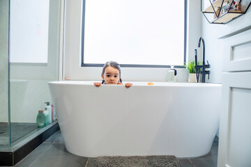 Toddler girl peering over the edge of bathtub