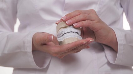 White jaw of crooked teeth made of plaster in the hands of an ortadont. Close-up of a dentist's hand showing a presentation on bite correction in children and adults. Clinical trials in hospitals