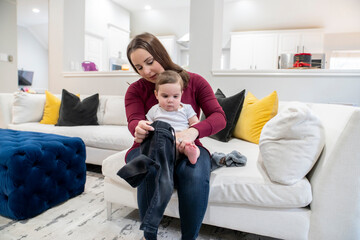 Mom changing baby boy's clothes on couch in home living room 