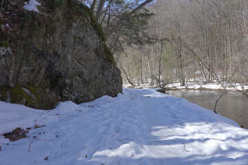 snow covered road between a cliff and a river