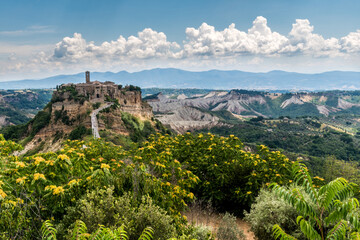 Civita 01 - borgo antico su sperone di tufo con fiori gialli, calanchi montagne e nuvole