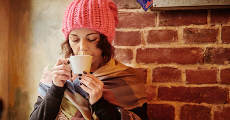 close up winter portrait of a happy and beautiful young lady in a pink knitted beanie hat. She drink coffee