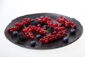 Fresh red currant, blueberries and dewberries on handmade black clay plate