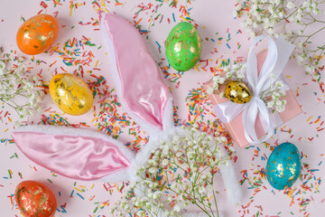 The minimal concept of Easter. An Easter card with a copy of the place for the text. Bunny ears colored eggs and flowers on a pink background. A copy of the space. Top view. Flat lay