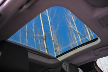 Blue sky and forest trees trough and open car sunroof. Closeup. Open hatch on a roof of the modern...