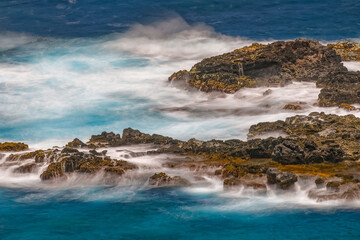 Long exposure on surf along rocky beach, Maui, Hawaii.