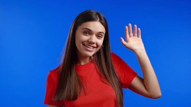 Young friendly woman waving hand - goodbye, chao, adios. Parting, say bye to camera. Beautiful trendy girl waving hand on blue studio background. 4k