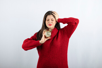 Young beautiful brunette woman holding an alarm clock standing 