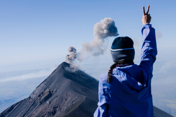 Climber celebrating at the top of the Acatenango volcano observing the volcano of fire in Guatemala - female hiker with raised hand with sign of love and peace © Fernanda