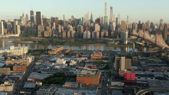 Aerial zoom in shot of bridge over East River amidst buildings in city, drone flying over structures during sunset - New York City, New York