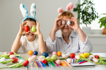 Easter concept. Grandmother with granddaughter are holding Easter eggs at home