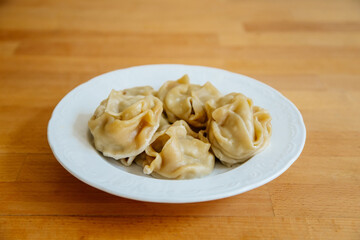 Delicious stuffed dumplings on white plate on wooden table desk. Asian manti or manty of dough and minced with lamb meat, prepared boiled, National traditional Tatar, Kazakh, Uzbek cuisine