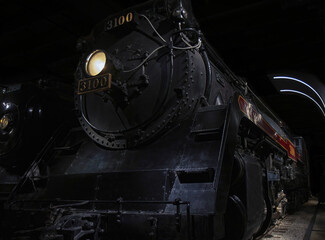 Massive black vintage steam locomotive at railway platform headlight on at night nobody