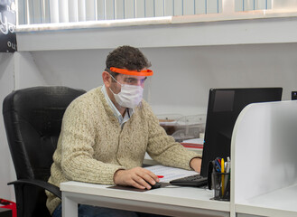 Fototapeta na wymiar Man working in the office during the pandemic period. Ways to be protected from Covid19. with mask and visor