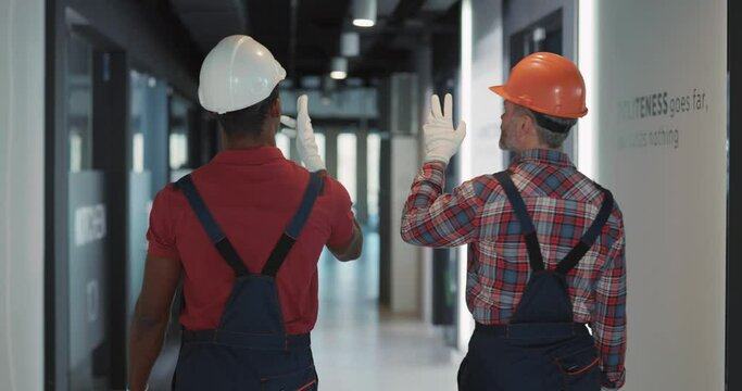 Multi-ethnic repair services couple of electrician and adult engineer walking inside residential building to control lighting electric system.