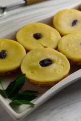 Potato Mud Cake or Kue Lumpur Kentang, Indonesian traditional cake made from potato, flour, eggs topping with raisin. Served on white ceramic plate and garnished with pandanus leaves. Bright photo.