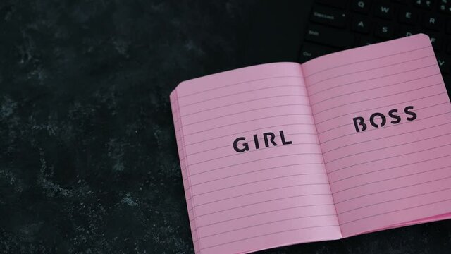 equal opportunities Girl Boss text on top of pink notebook on laptop keyboard on black background