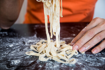 Preparing homemade fettuccine on a wooden maza. traditional cutting concept of Italian cuisine, cutting raw dough into tagliatelle on copy space