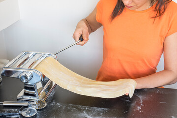 Fototapeta premium Woman roll out pasta dough with machine at home. making pasta 