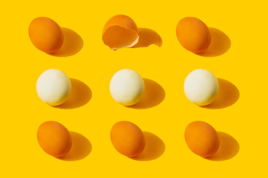 Chicken fresh and boiled eggs pattern with one empty broken eggshell on yellow background. Healthy food or Easter creative minimal concept. Flat lay