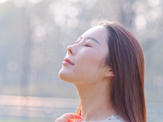 Close up portrait of beautiful young Chinese woman, head up with eyes closed in sunny light, head shot side view.