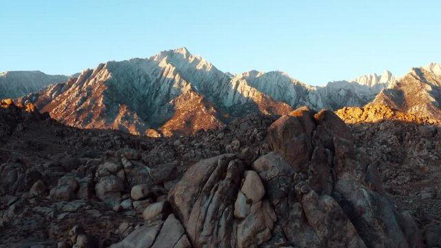 Aerial shot of rocks at famous natural landmark against blue sky, drone ascending near rocky mountains on sunny day - Alabama Hills, California
