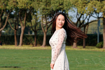 Beautiful Chinese woman with black long hair smiling and turning back with her flying hair in wind...