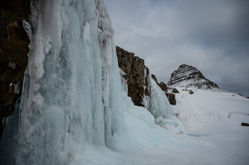 Fototapeta na wymiar frozen waterfall and snow covered mountain in Iceland